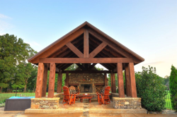 Rough cedar cabana structure with decorative accent beam, a metal roof, and a stacked stone fireplace